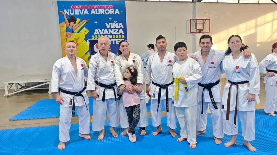 Grupo de karatecas reunido sobre un tatami azul en un gimnasio.