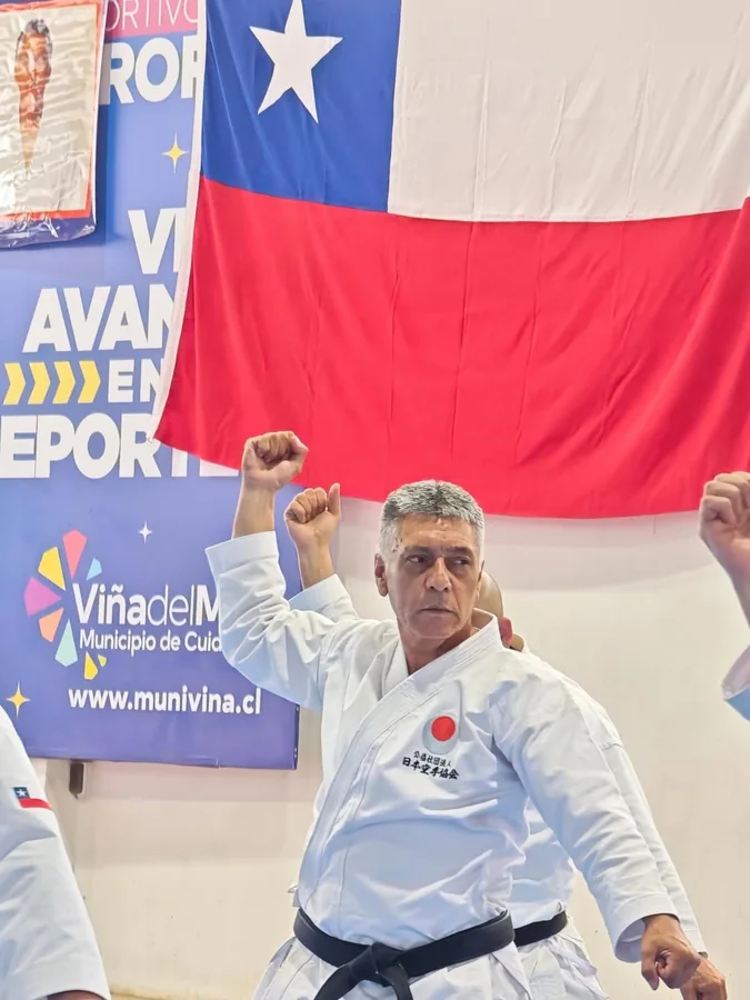 Practicante adulto de karate ejecuta una técnica frente a una bandera chilena.