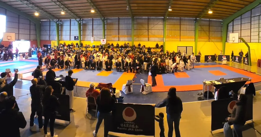 Vista general de un gimnasio con tatamis y público durante un encuentro de karate.